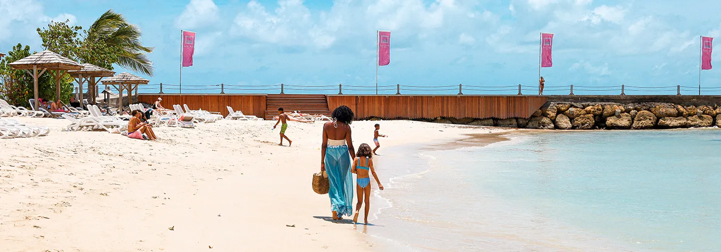 A complicit moment between a mother and her daughter walking on a tropical beach in Guadeloupe.
