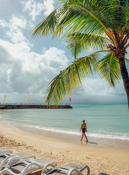 Frau geht an einem tropischen Strand entlang, der von Kokospalmen gesäumt ist, in Guadeloupe.