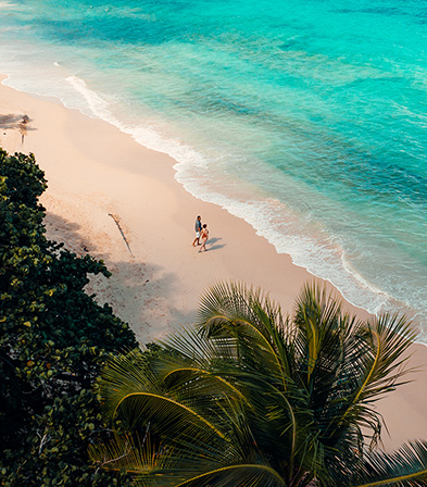 Luftaufnahme eines Paares, das an einem paradiesischen Strand auf Guadeloupe spaziert, für das 28-Tage-Kanada-Sonderangebot