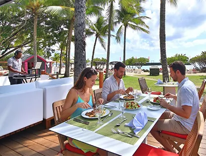 Un groupe de personnes partageant un repas sur la terrasse d'un restaurant en bord de mer, en écoutant un DJ