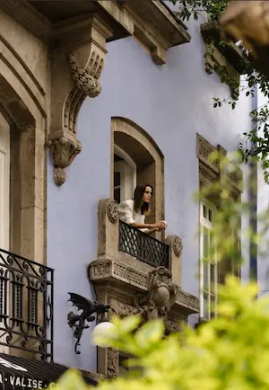 Smiling young woman in a white bathrobe stretching in a luxury bed at La Valise hotel.