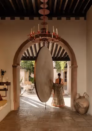 Woman from behind walking towards a monumental pink wall with Mayan-inspired sculptures at La Valise hotel.