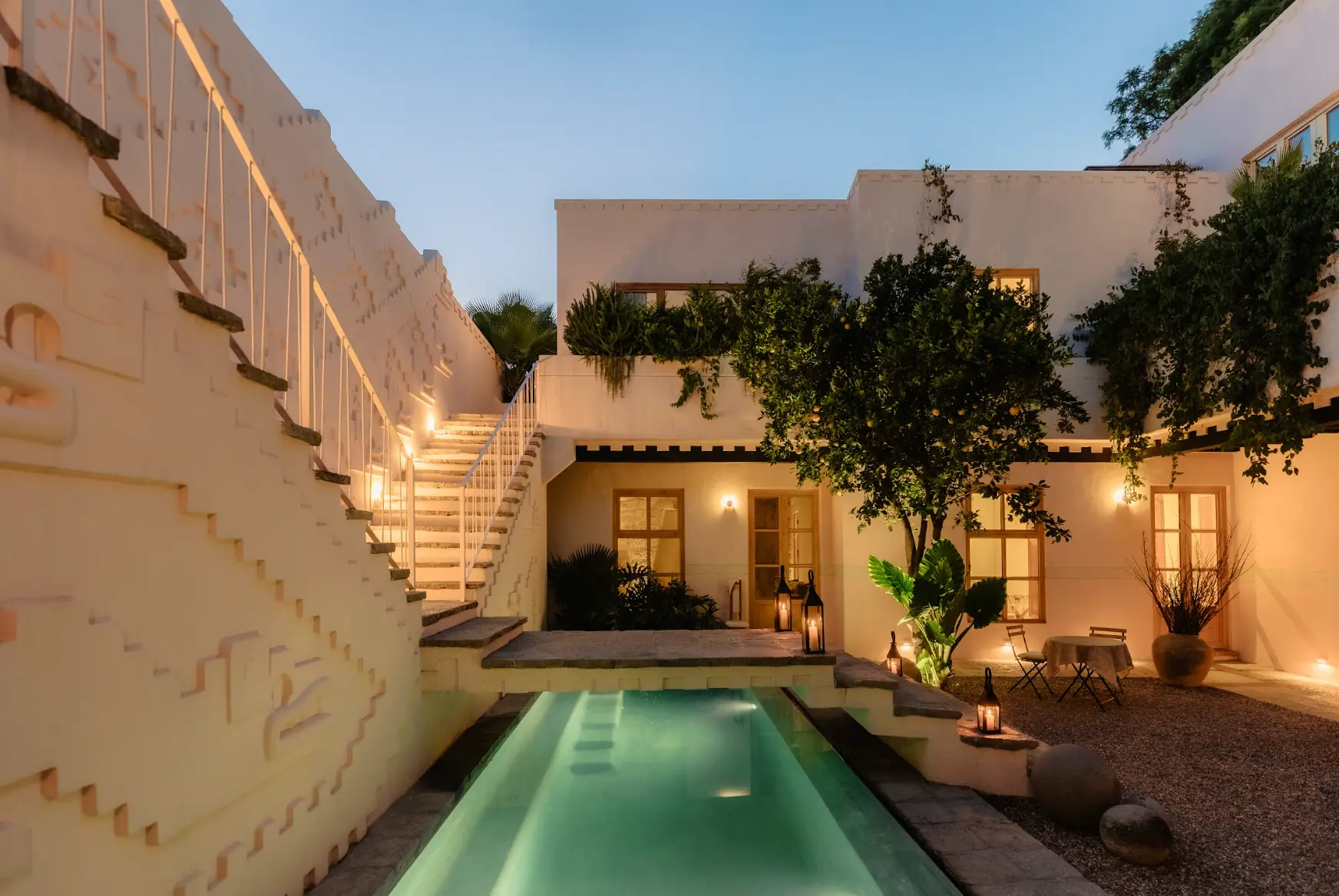 Luxurious inner courtyard at La Valise hotel featuring a narrow pool, tree, cafe tables, and pink colonial-style architecture.