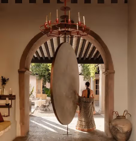 Woman from behind walking towards a monumental pink wall with Mayan-inspired sculptures at La Valise hotel.