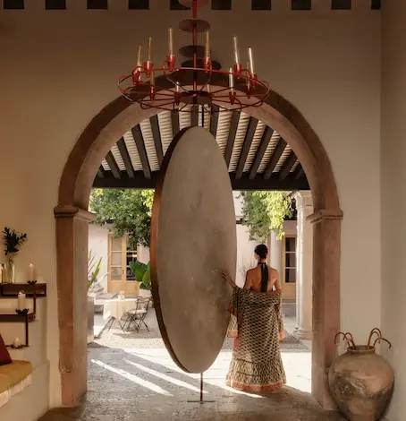 Woman from behind walking towards a monumental pink wall with Mayan-inspired sculptures at La Valise hotel.
