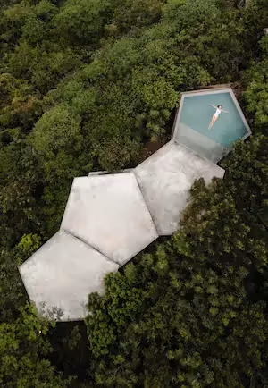 Aerial view of a luxury villa with minimalist design featuring an infinity pool and clean lines, surrounded by a lush natural landscape.