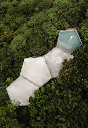 Aerial view of a luxury villa with minimalist design featuring an infinity pool and clean lines, surrounded by a lush natural landscape.