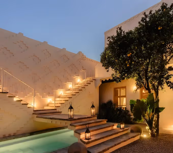 Luxury villa courtyard at twilight featuring an illuminated swimming pool, stone outdoor staircase, and traditional lanterns.