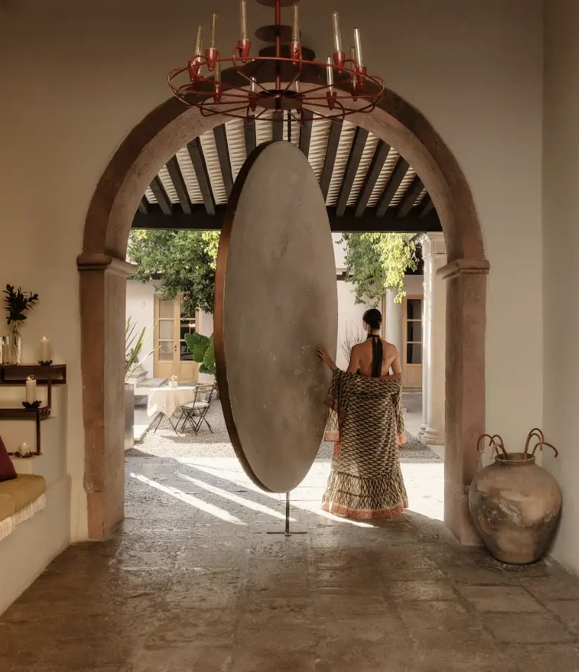 Woman from behind walking towards a monumental pink wall with Mayan-inspired sculptures at La Valise hotel.