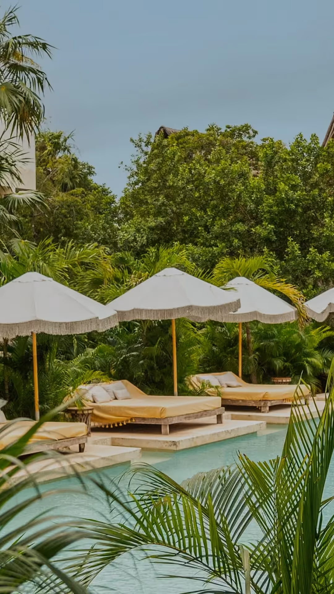 Luxury swimming pool lined with white umbrellas and tropical greenery featuring a thatched-roof villa at La Valise hotel.