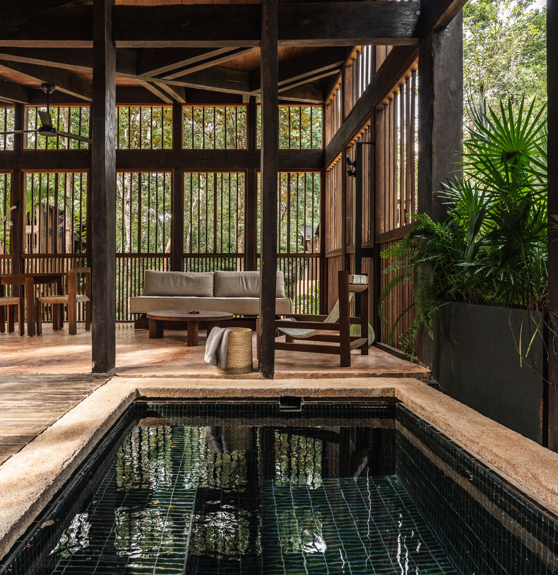 Modern rustic outdoor deck with dark tile plunge pool and open-air seating area surrounded by trees.