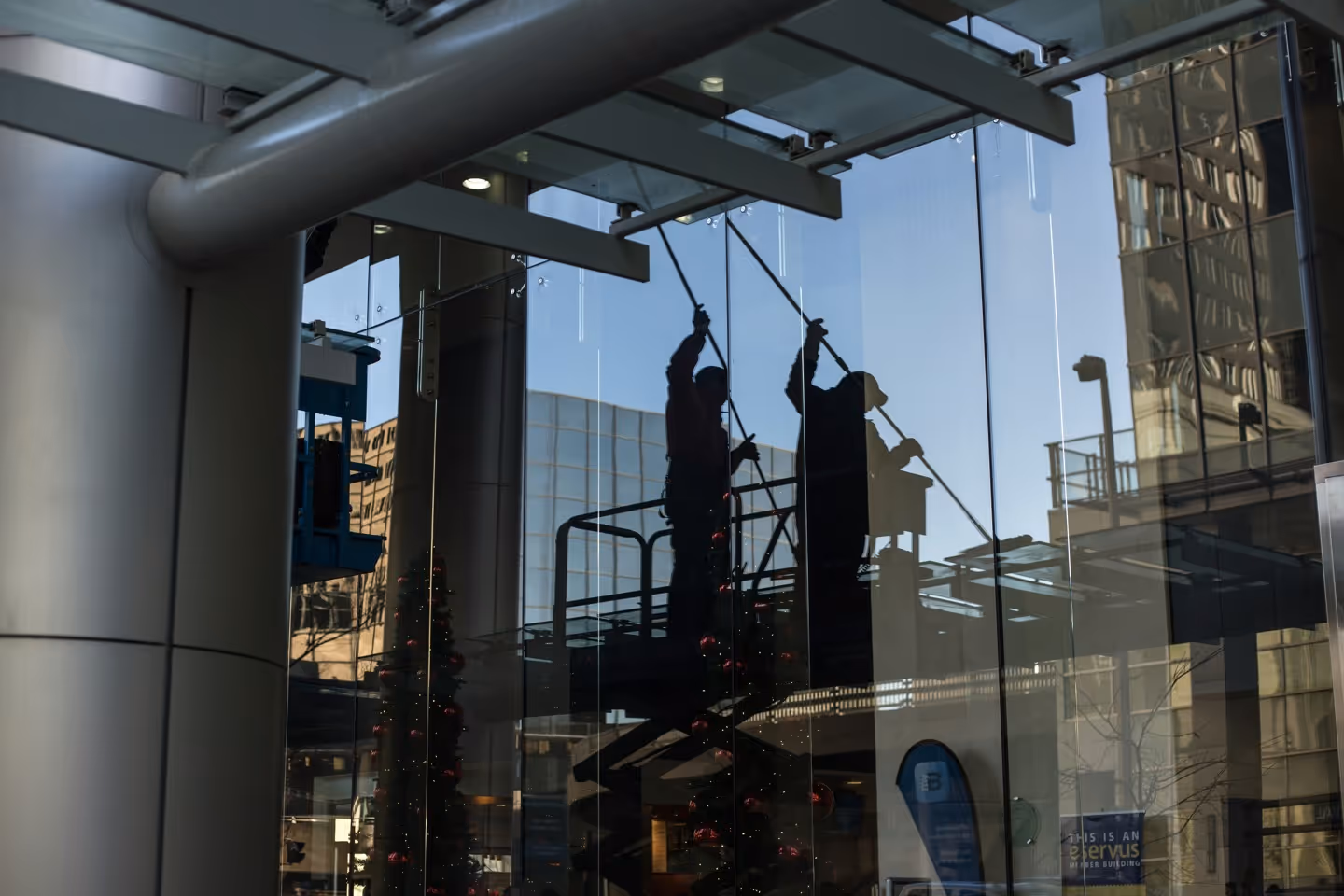 Spiegelung von Fensterreinigern auf einer Hebebühne beim Reinigen großer Glasfassaden eines modernen Gebäudes.