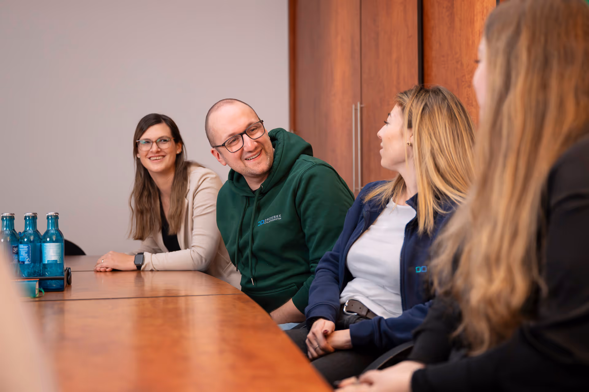 Vier Personen sitzen an einem Konferenztisch, unterhalten sich lächelnd und wirken entspannt.