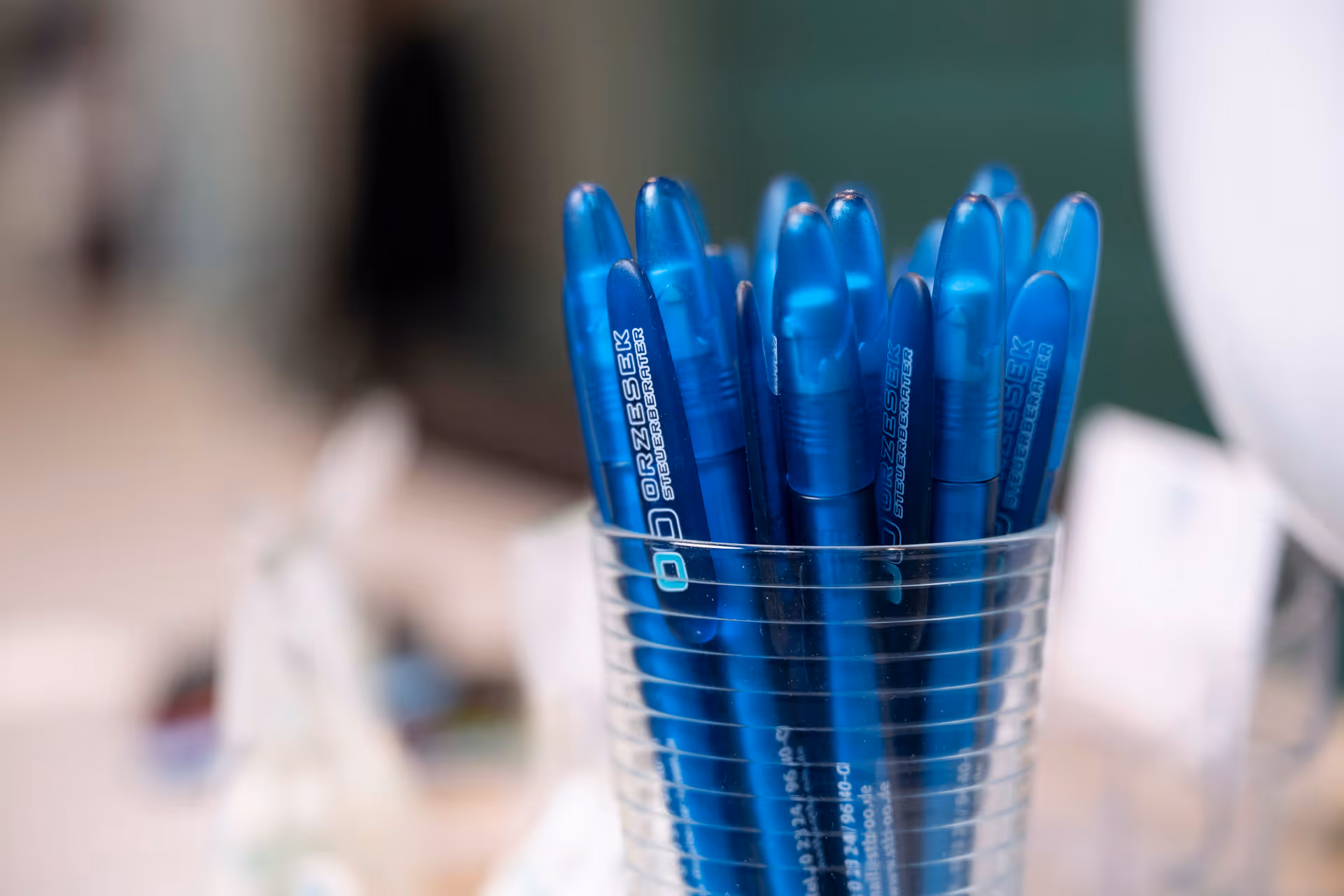 Mehrere blaue Kugelschreiber mit Orzesek Aufdruck in klarem Glas auf einem Tisch.