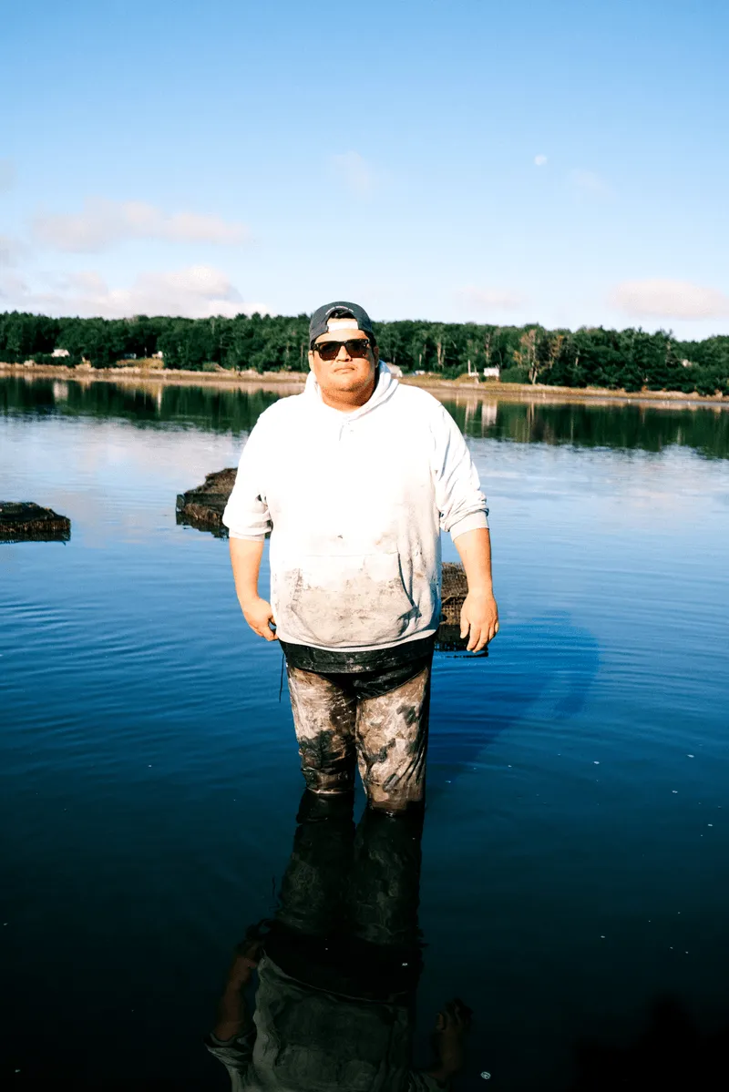 A man wading in the ocean at an oyster farm.