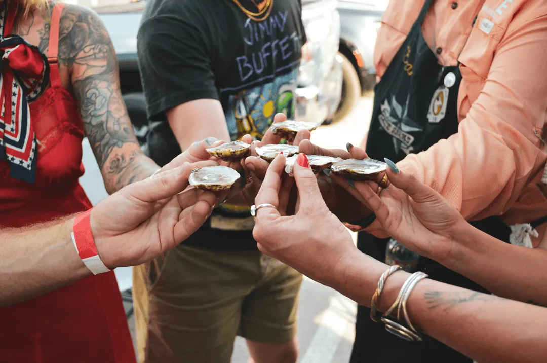 A group of people holding up their hands with oysters in them at an event.