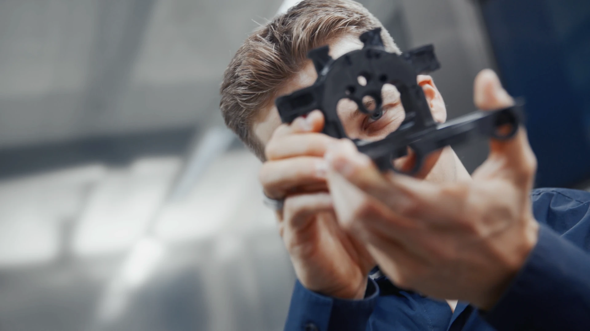 Man examining a black mechanical part closely while holding it with both hands.