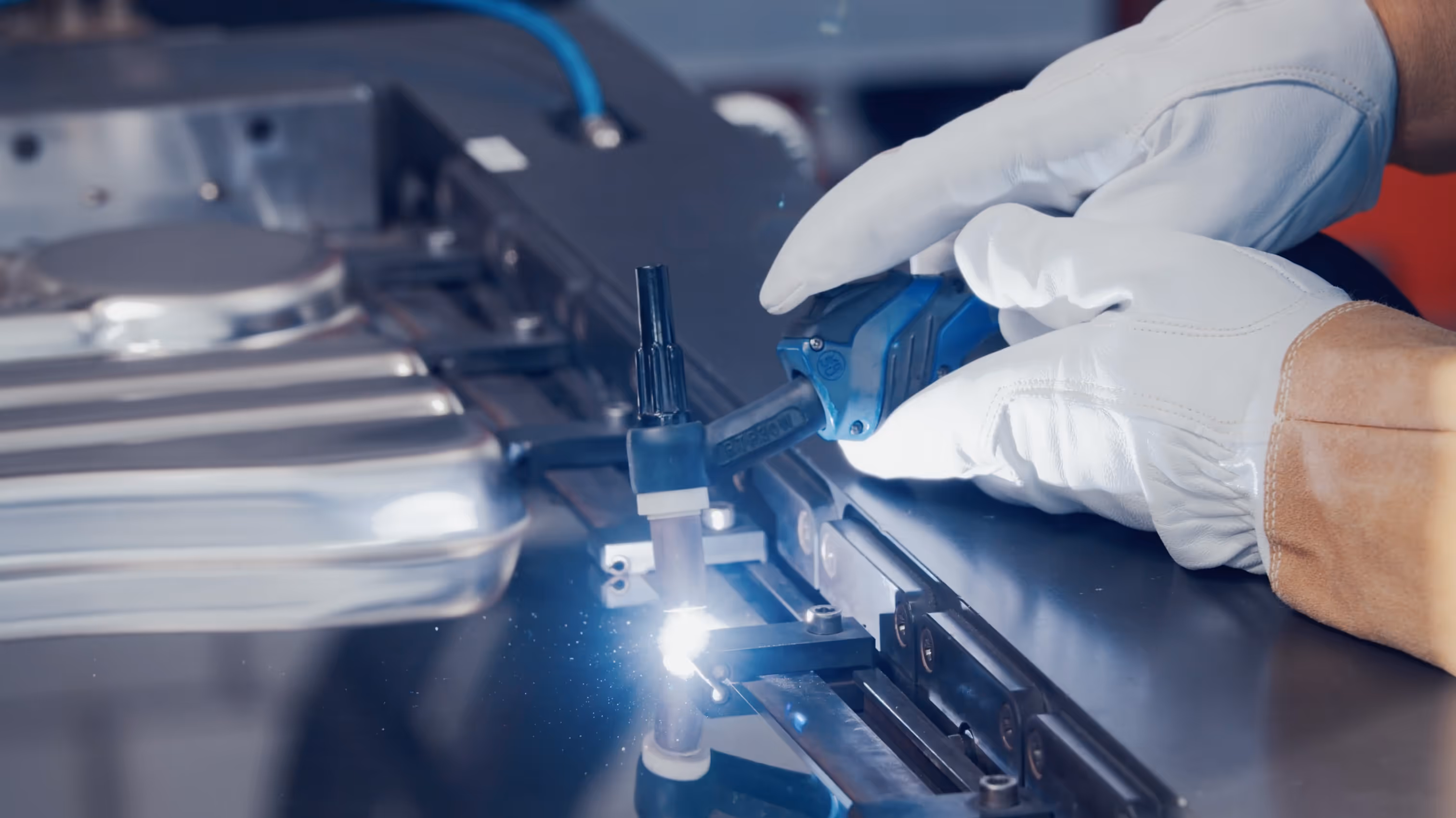 Gloved hand holding a welding torch emitting a bright spark during metalwork on industrial equipment.