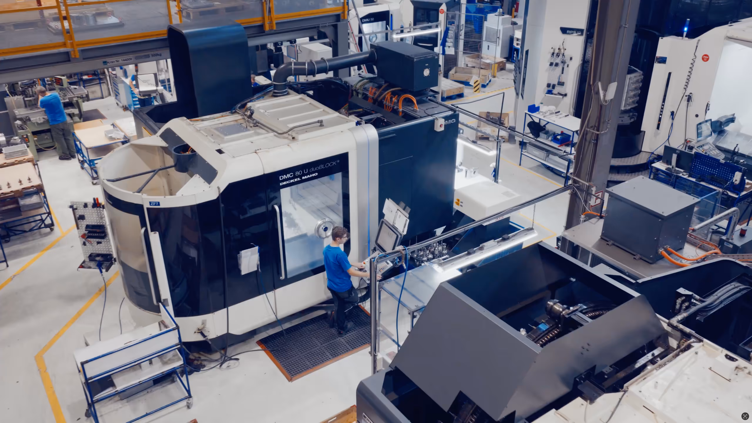 Worker operating a large CNC machine in a clean, high-tech industrial manufacturing facility.