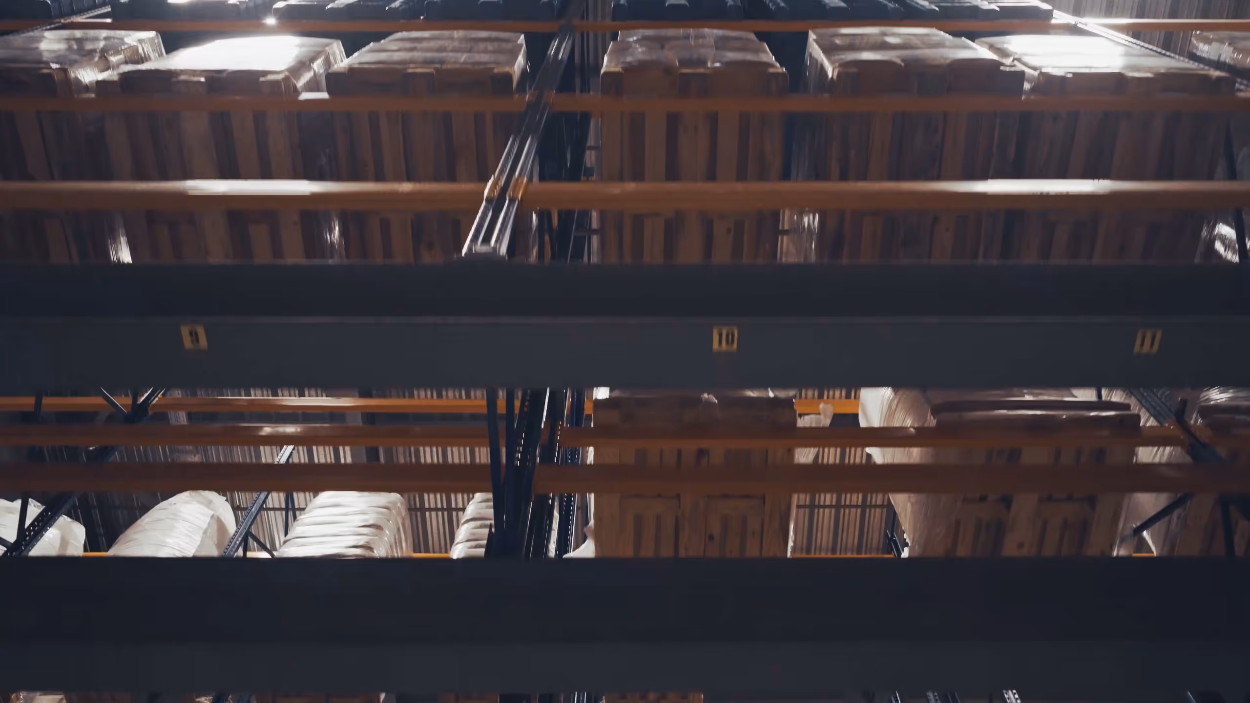 View looking upward at tall industrial warehouse shelving filled with stacked pallets wrapped in plastic.