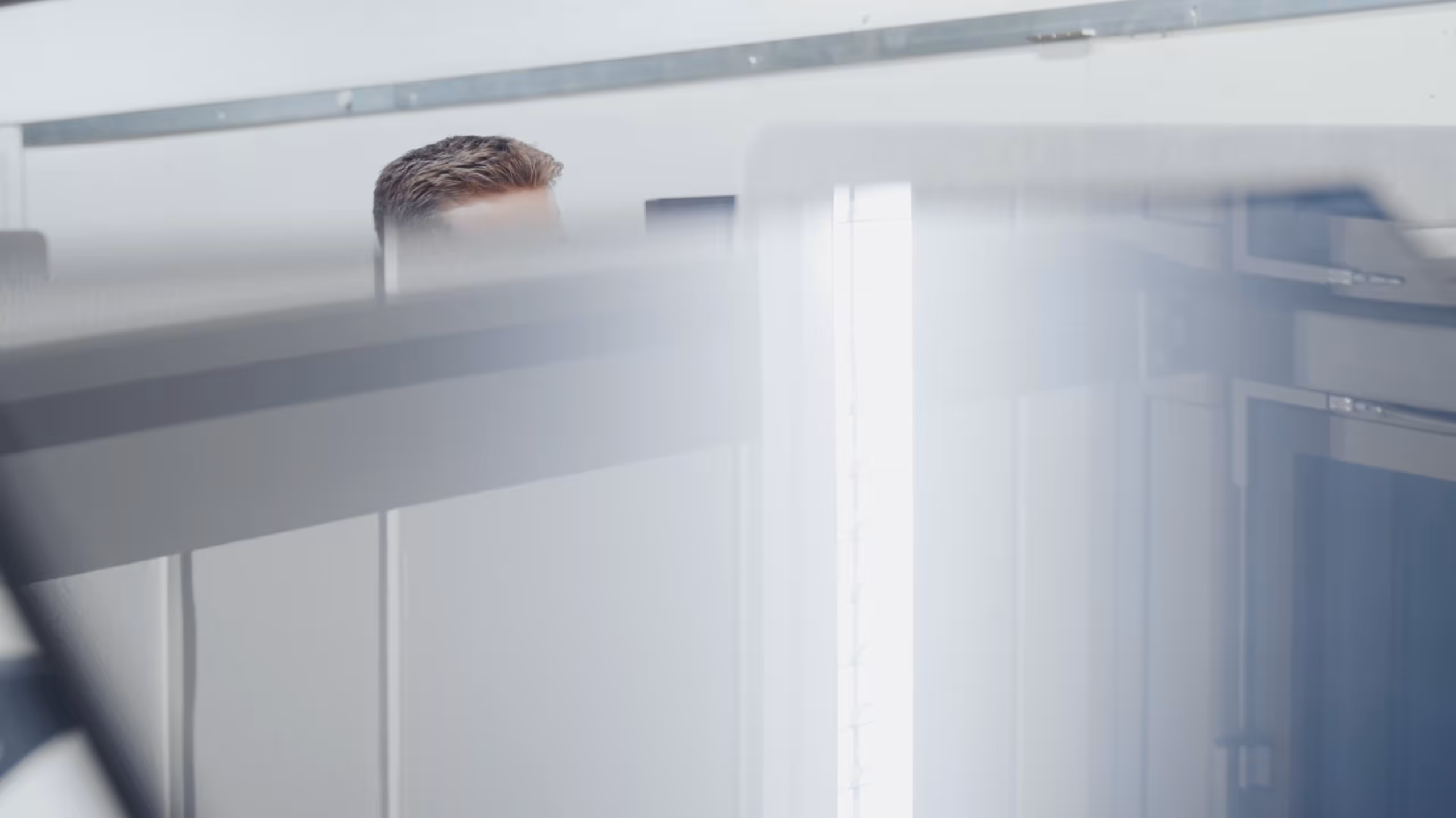 Man with short hair partially visible behind blurred glass office partitions.