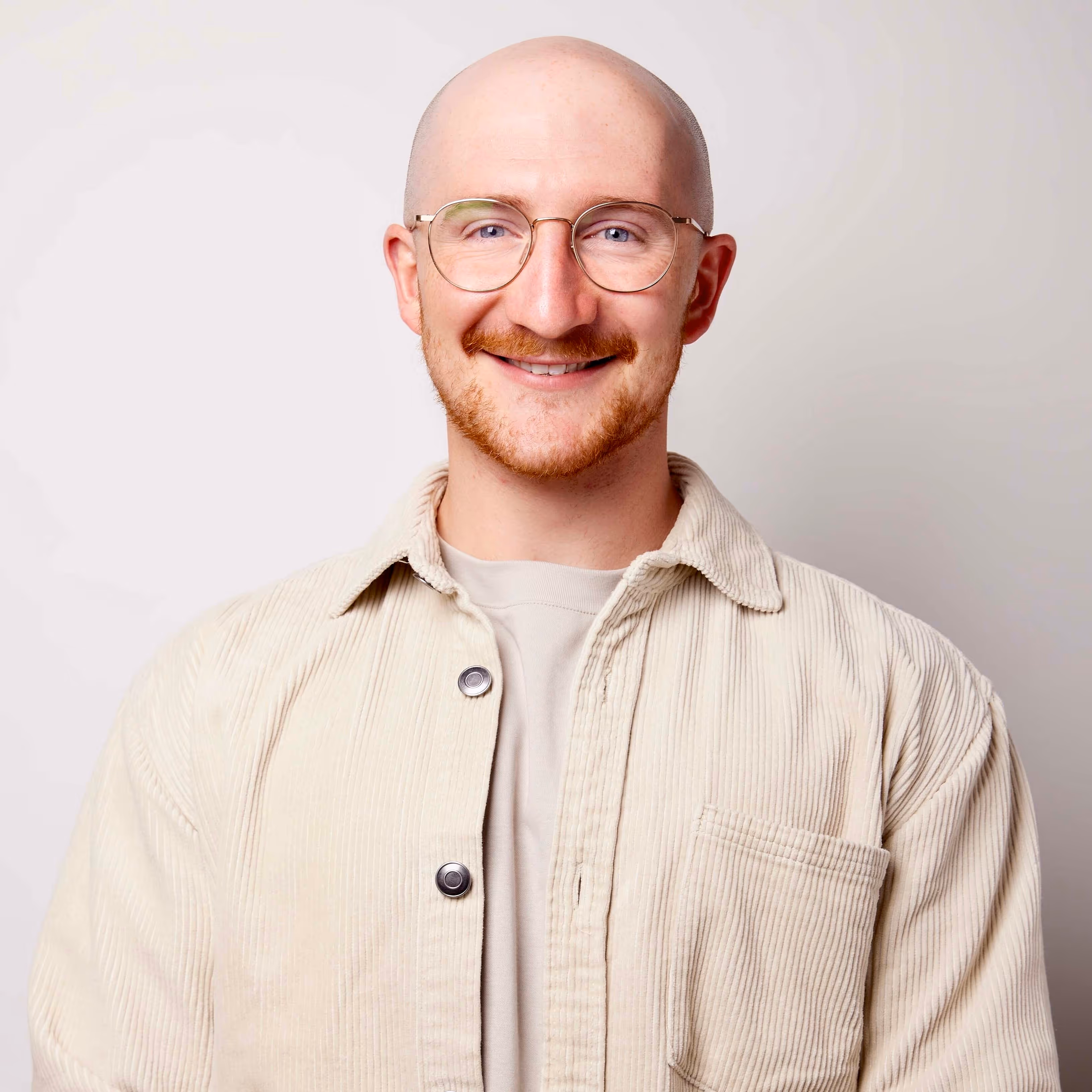 Smiling bald man with glasses wearing a light beige corduroy shirt over a beige t-shirt.