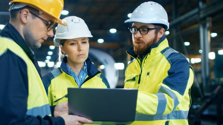 Three workers in safety gear examine a laptop together, showcasing teamwork and dedication to their task.