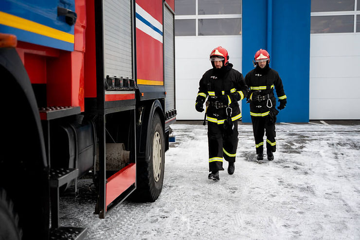 Two firefighters dressed in protective gear walking next to a fire truck, prepared to tackle a fire emergency.