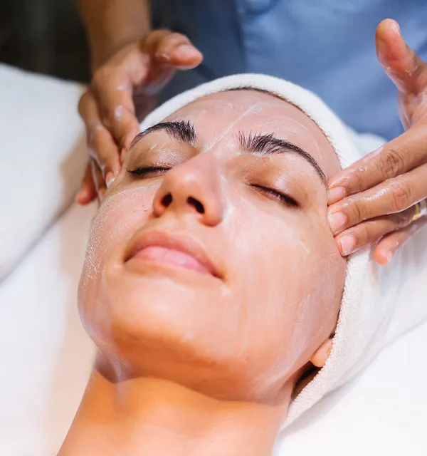 Person receiving a facial massage with cream applied on their face and eyes closed.