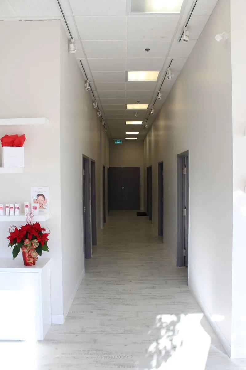Bright, narrow hallway with white walls, light wood flooring, and dark door frames on both sides leading to a closed double door.