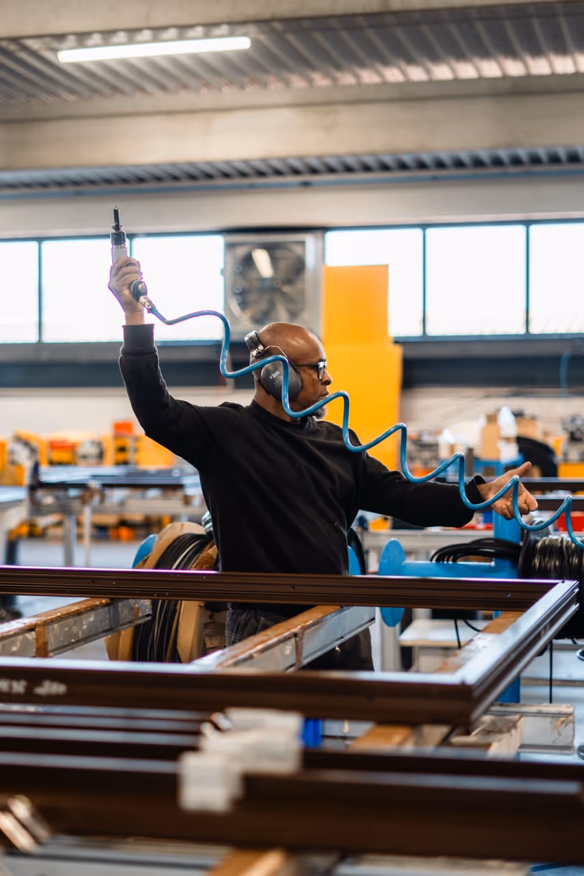 Un homme devant un établis manipulant une visseuse devant un chassis de fenêtre