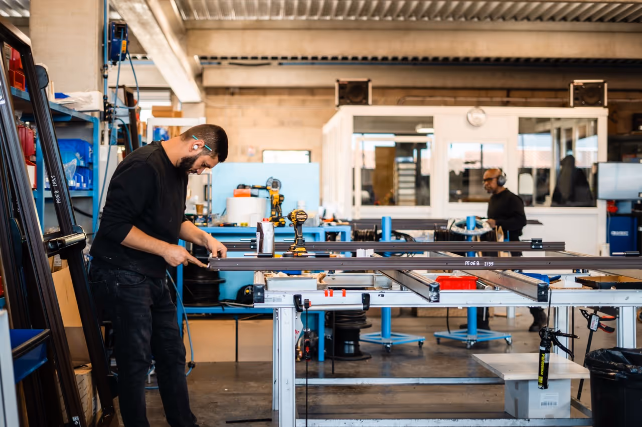 un homme en train d'ébavurer le chassis d'une fenêtre sur une zone d'assemblage