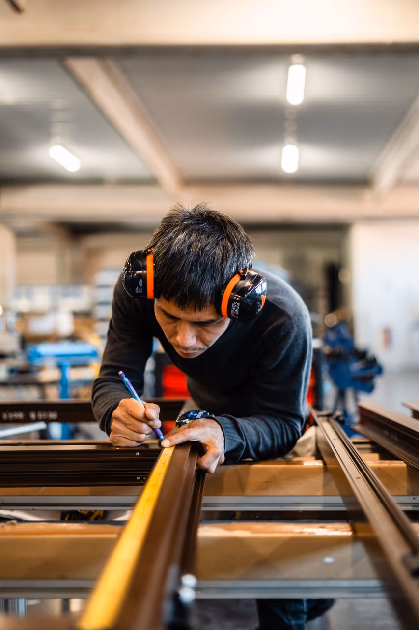Un homme vue de prêt qui trace des mesure avec un mètre et un crayon sur le chassis d'une fenêtre en aluminium