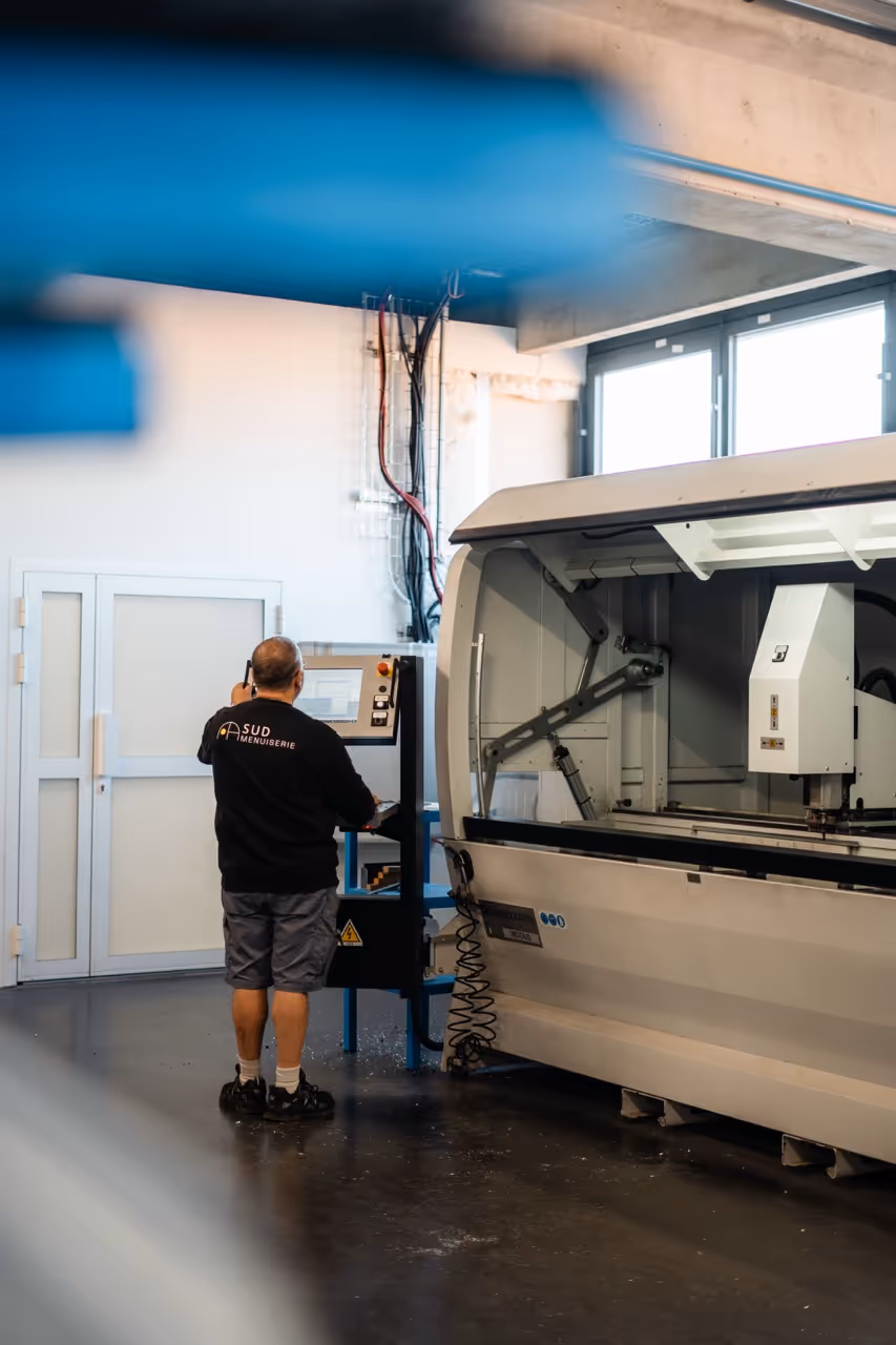 Un homme installé devant une grande machine de découpe laser, en train de configurer la machine sur un moniteur positionné à côté