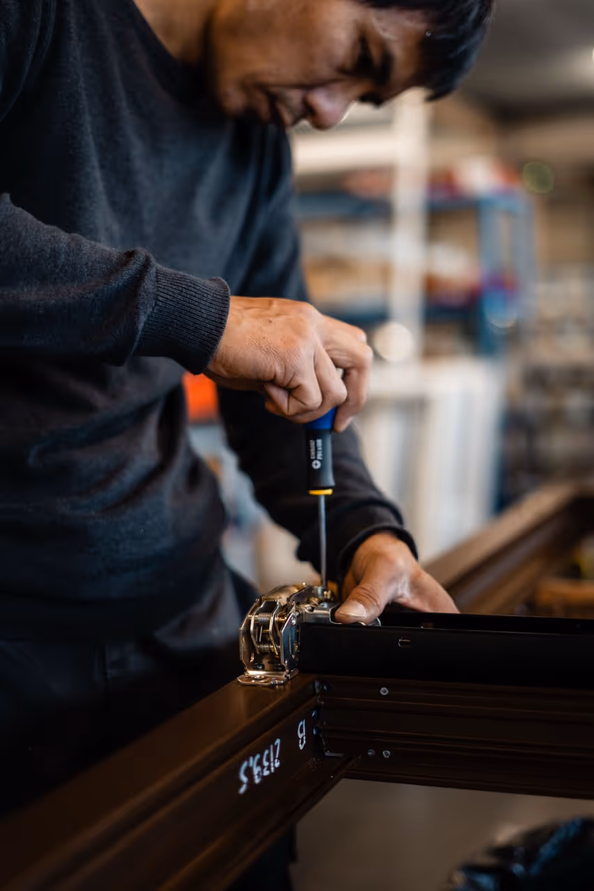 Vue de prêt d'un agent réglant un chassis de fenêtre noir à l'aide d'un tournevis sur les éléments de jonction du cadre