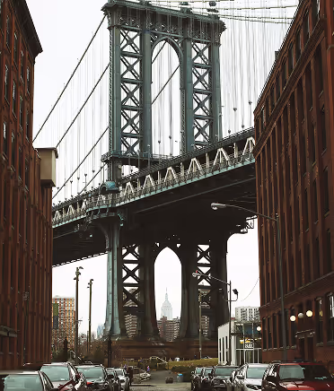 View of the Manhattan Bridge framed by red-brick buildings in Dumbo, Brooklyn, with the Empire State Building visible in the distance.