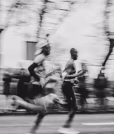 Black and white blurred photo of two runners in motion during a race on a street lined with trees.