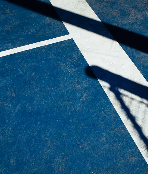 Shadow of a basketball hoop and net cast onto a blue basketball court with white boundary lines.