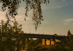 Bridge spanning over a river surrounded by trees with a cloudy sky at sunset.