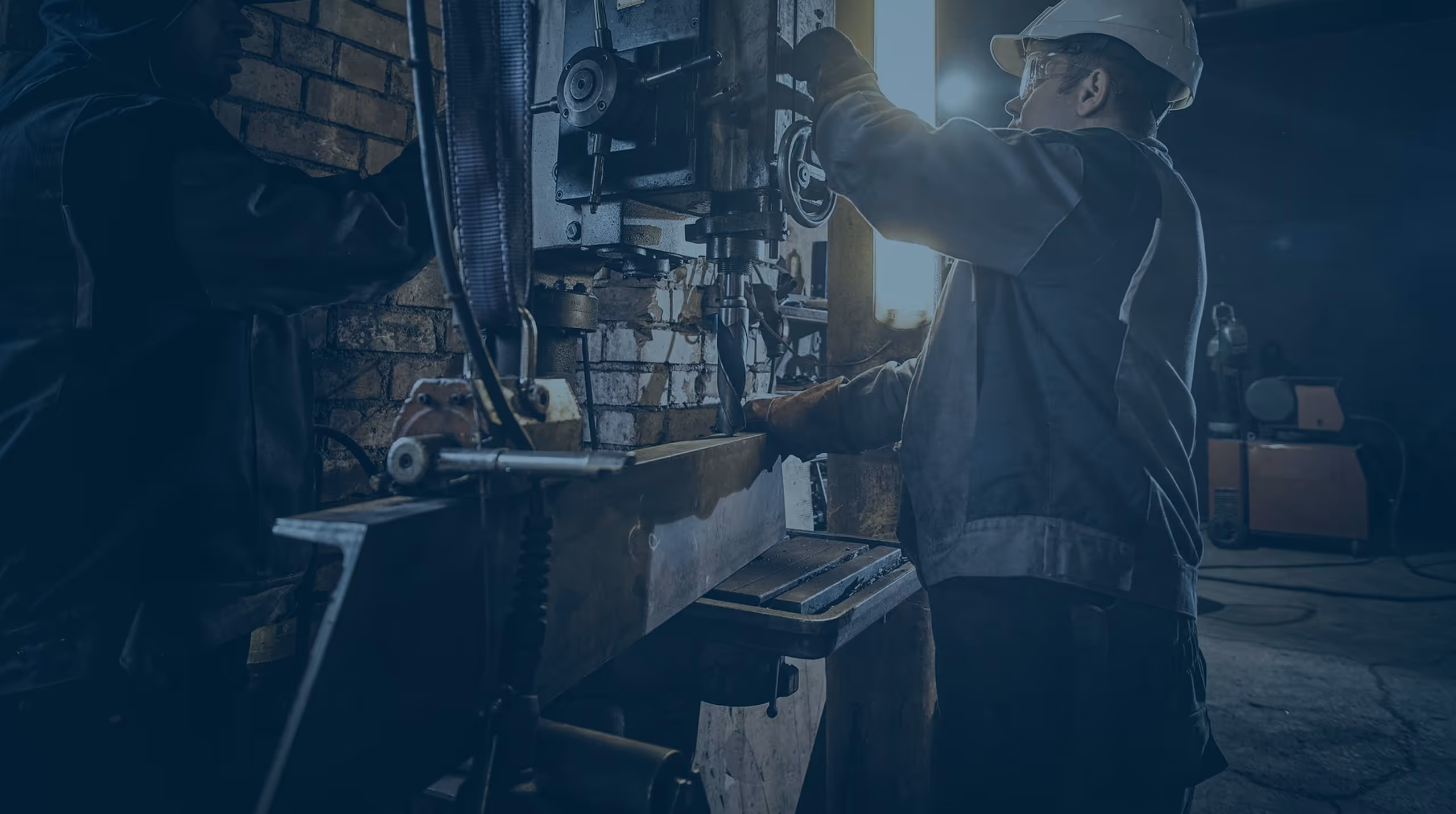 Worker wearing safety helmet and gloves operating industrial drilling machine in a workshop.