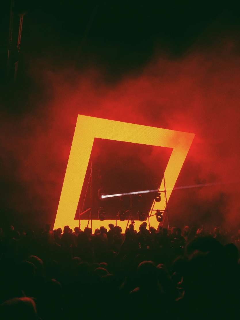 A rave stage set with a large orange glowing neon square above the crowd