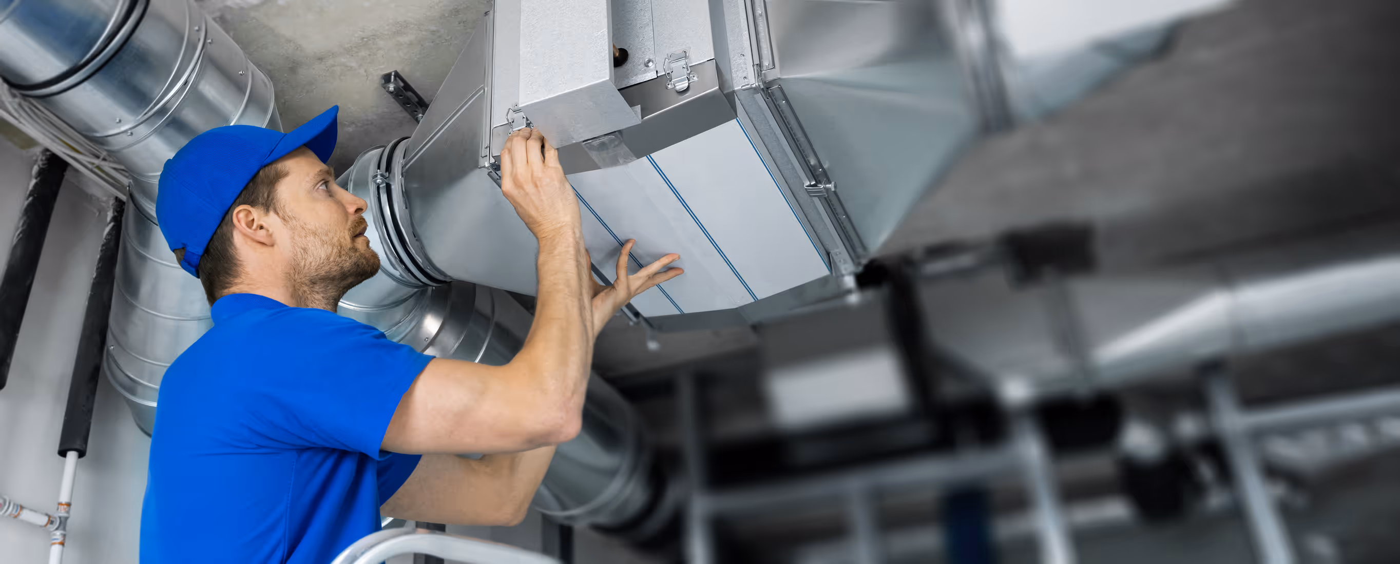 Male technician in blue uniform inspecting and adjusting ventilation ducts.