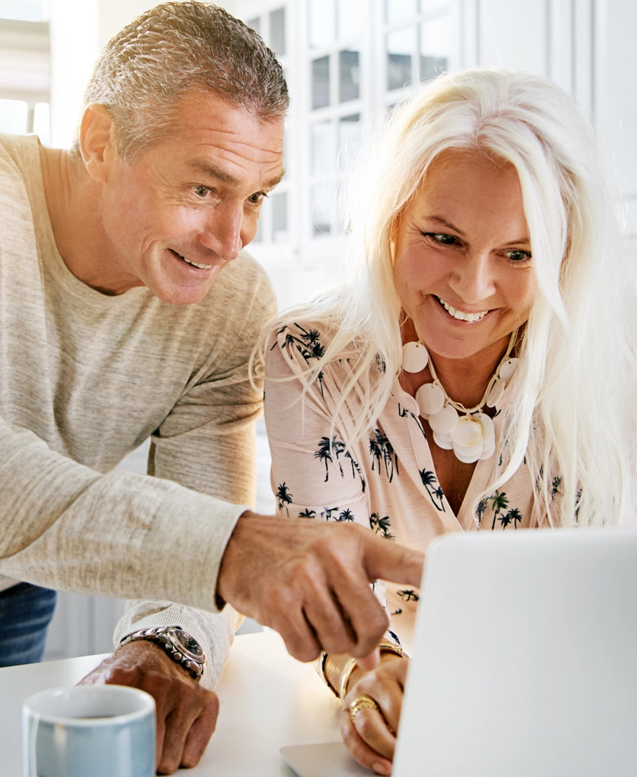 Smiling mature man and woman looking at a laptop screen together in a bright room.
