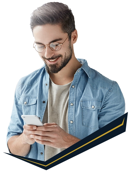 Smiling man with glasses and a beard wearing a denim shirt using a smartphone.