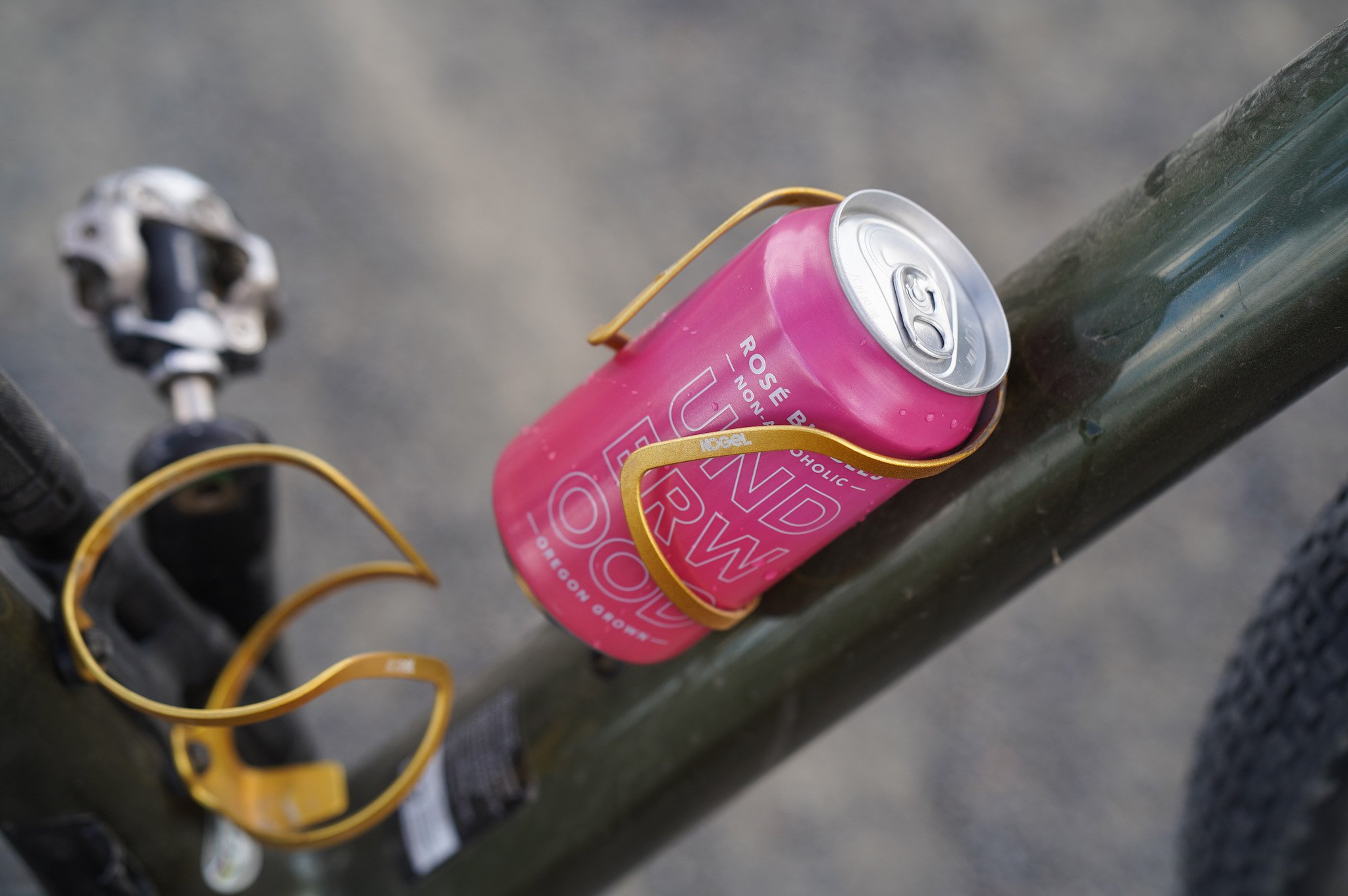 Pink can of Underwood NA Rosé Bubbles held in a gold bicycle bottle cage on a green bike frame.