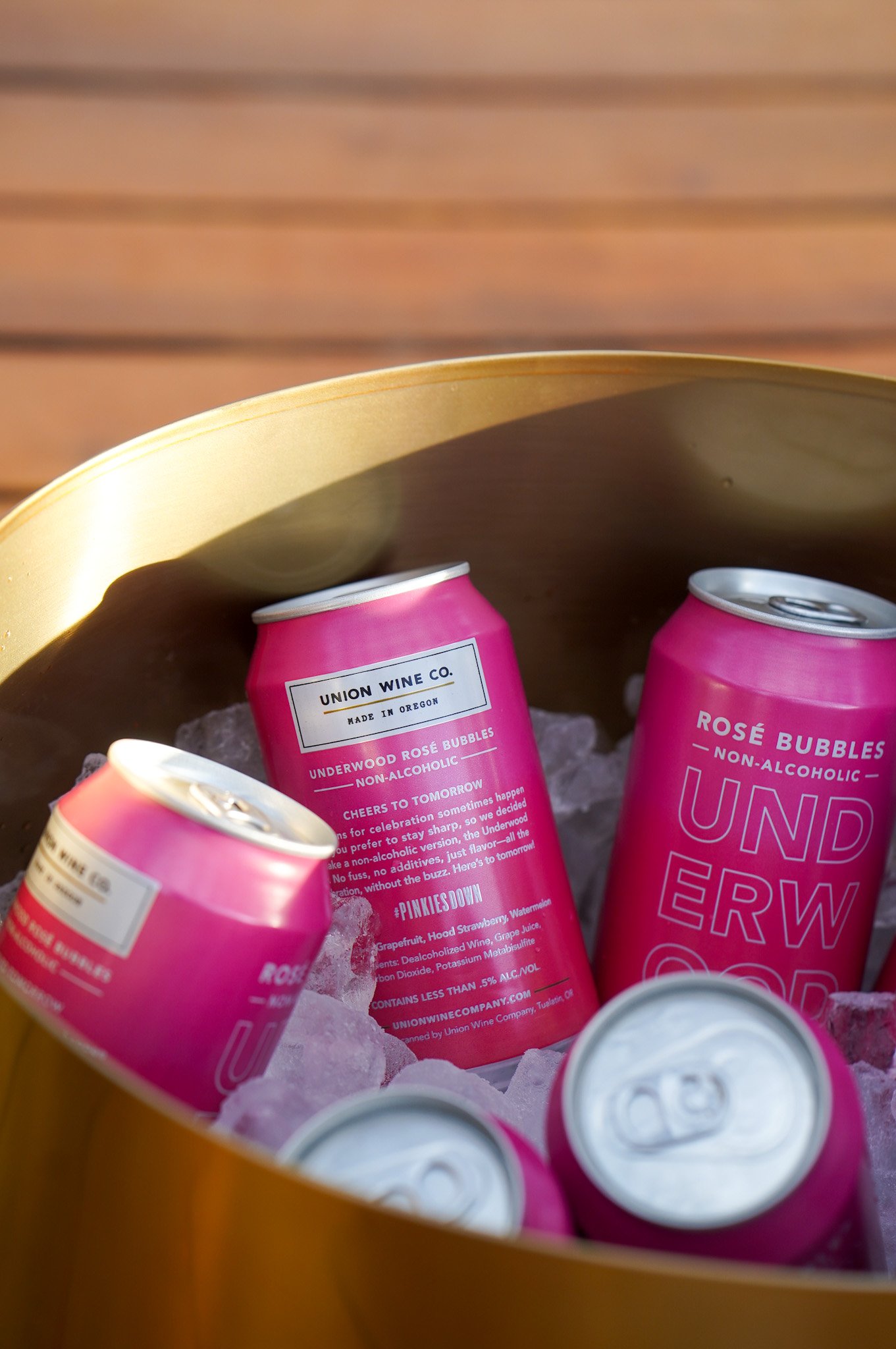 Pink cans of Underwood NA Rosé Bubbles chilling in a gold bucket filled with ice.