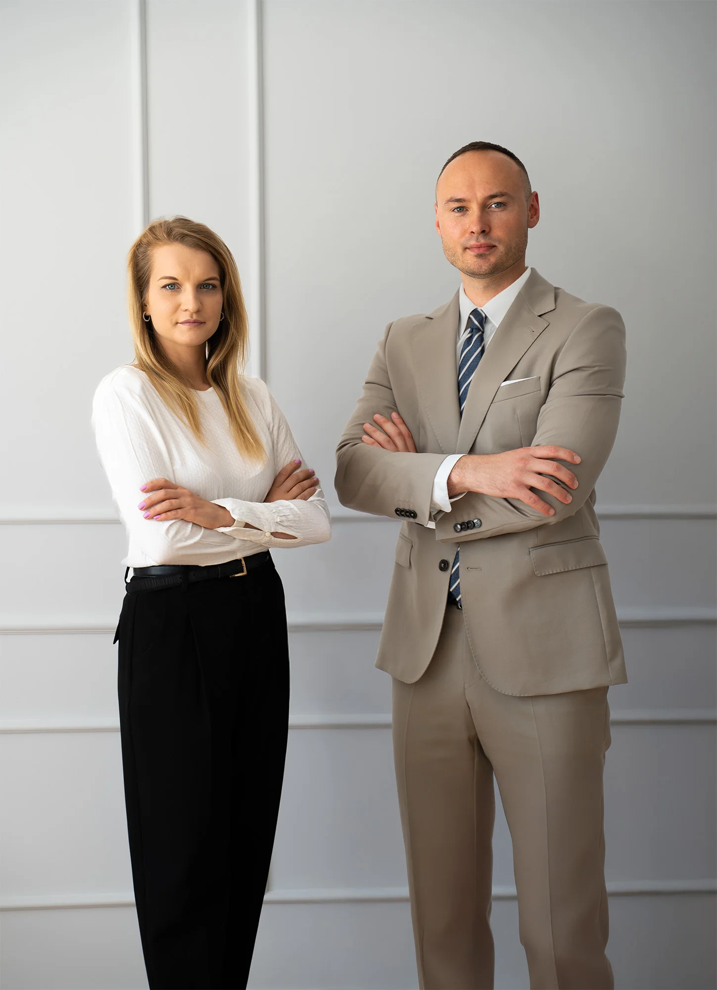 Profesjonalny mężczyzna w beżowym garniturze i kobieta w białej bluzce pozująca w nowoczesnym biurze