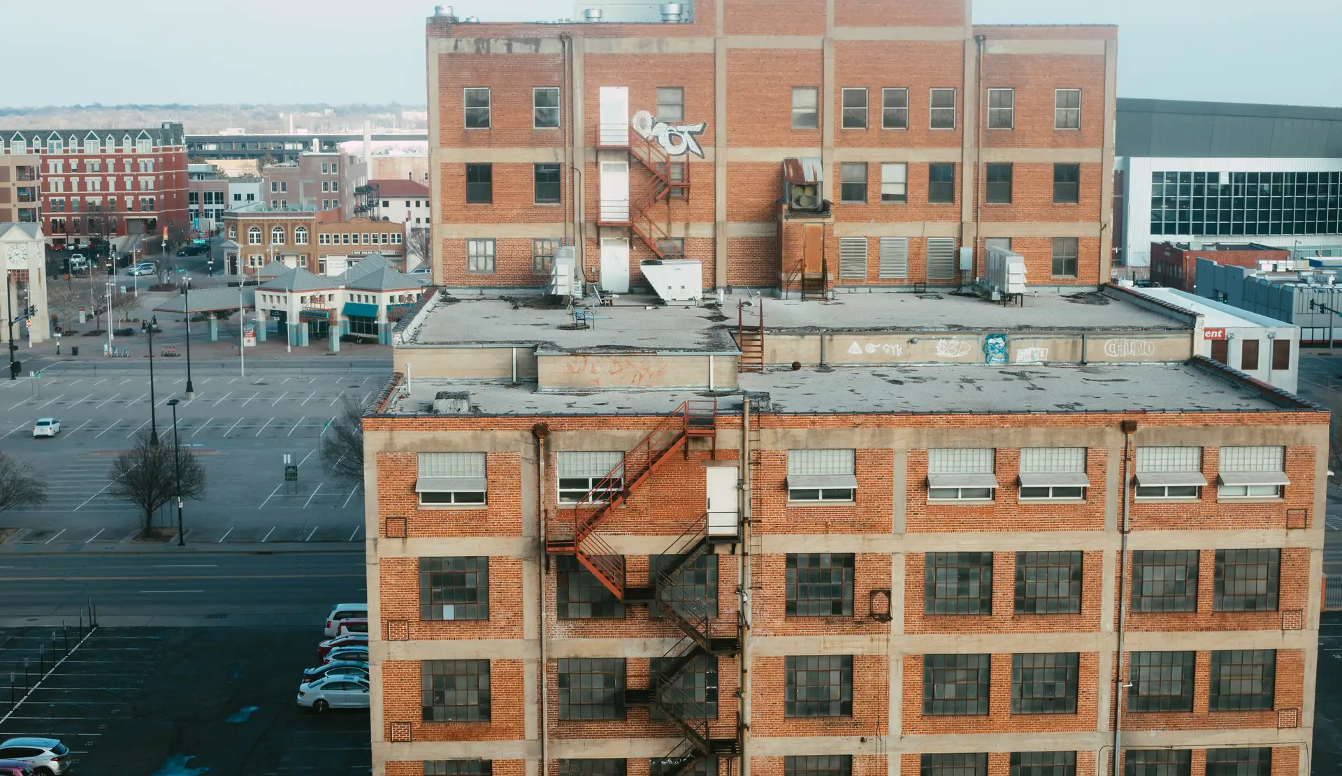 Multi-story brick building with industrial windows and external metal fire escape stairs in an urban setting.