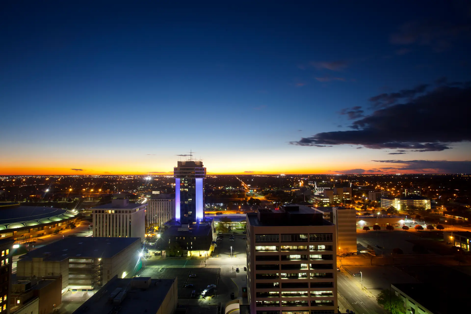 City skyline at dusk with illuminated buildings and a colorful sunset horizon.