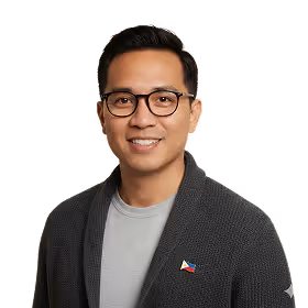 Smiling man wearing glasses, a gray cardigan with a Philippine flag pin, and a light gray shirt, against a black background.